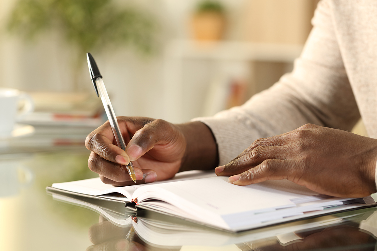 Lähikuva mustasta miehestä käsien kirjoittamassa muistutusta kalenteriin pöydällä kotona