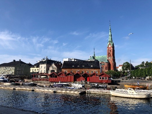 Maisema, jonka etualalla vettä ja vene. Taustalla on kirkko ja rakennuksia.