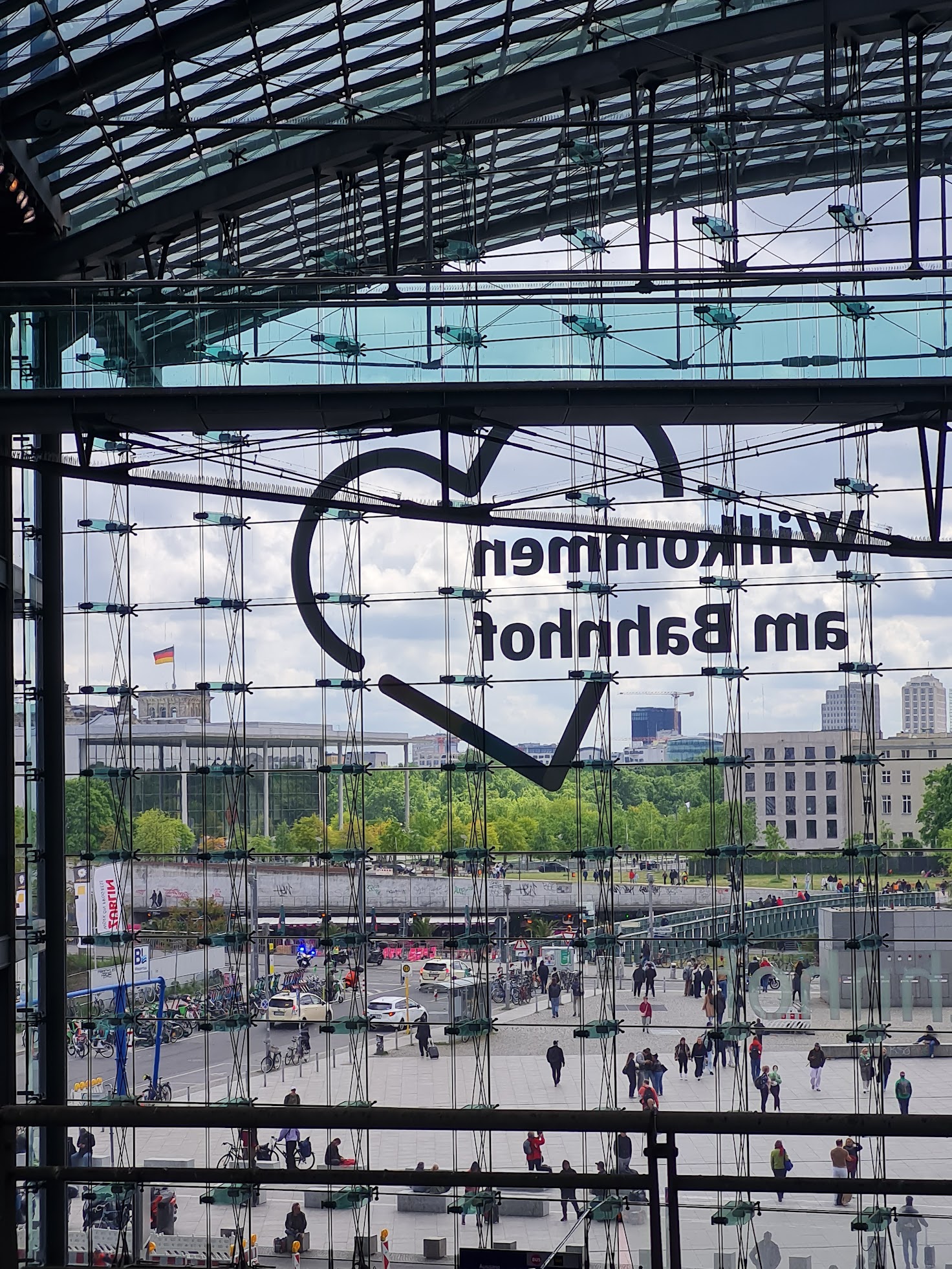 Kuva lasiseinäisen asemarakennuksen sisältä. Lasiseinällä lukee Wilkommen am Bahnhof ja sydän