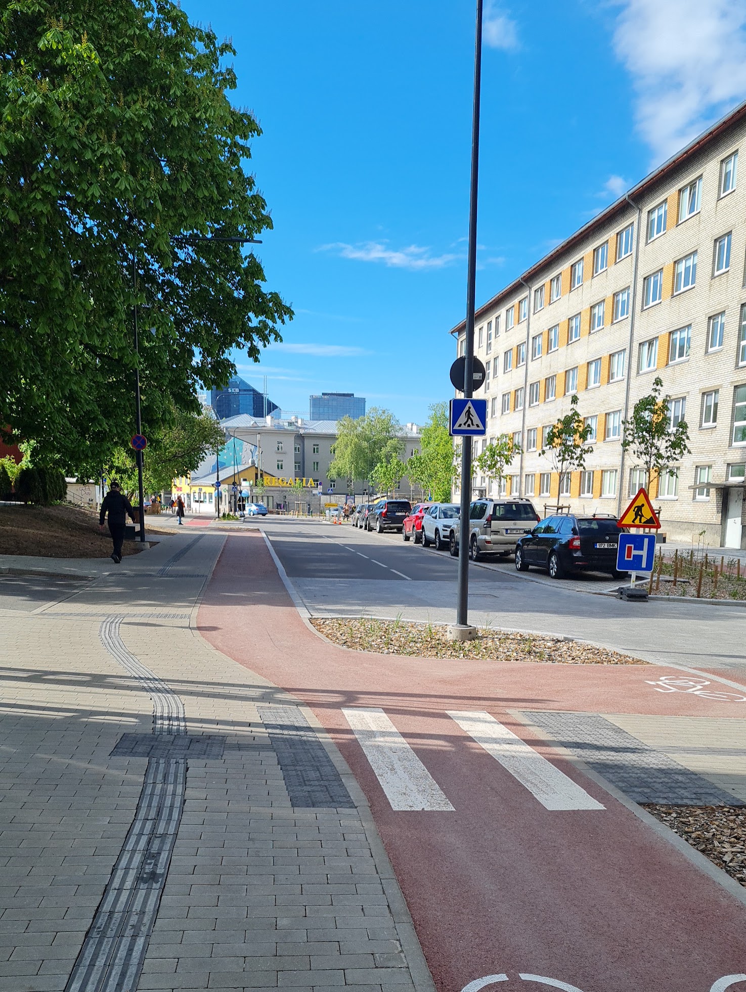 Taustalla on sininen taivas ja etualalla on kävelytie ja pyörätie ja sivulla vihreitä puita.